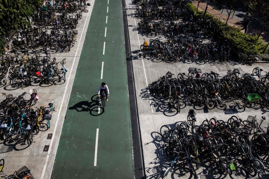 A man rides his bicycle past many other parked bicycles.