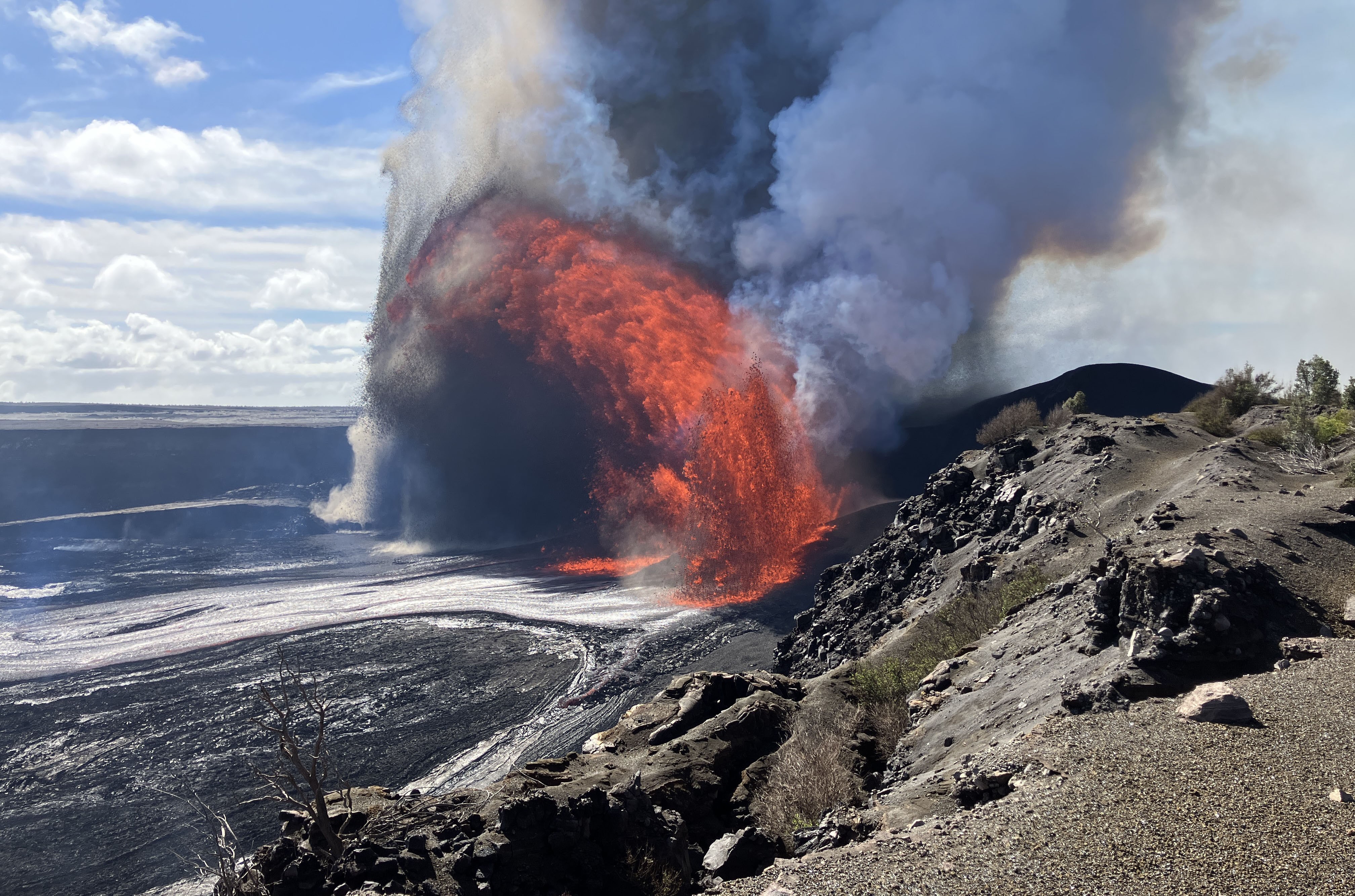 Lava shoots into the air, arcing above a broader crater floor, in Hawaii.