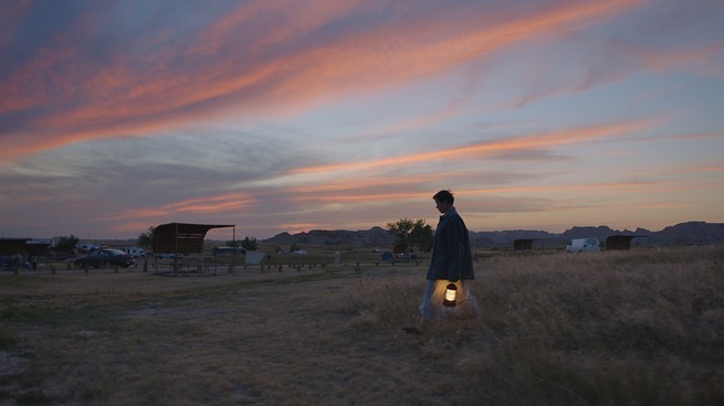 A woman walks through a field with a lantern in the movie "Nomadland"