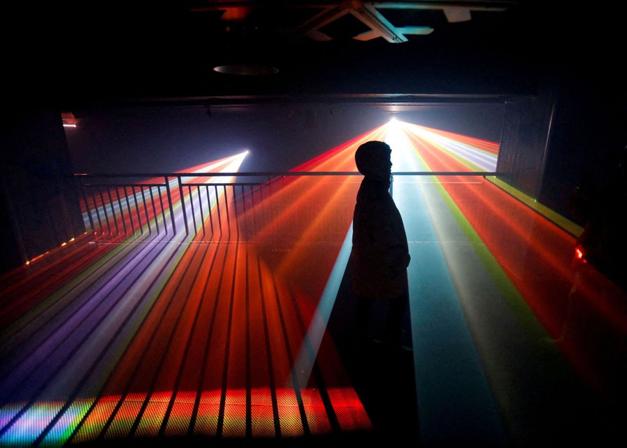 A person walks through a dark room as shafts of multicolored light are displayed around them