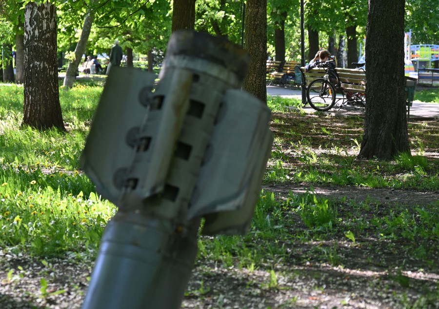 The tail fins of a missile embedded in the ground in a city park, with benches nearby