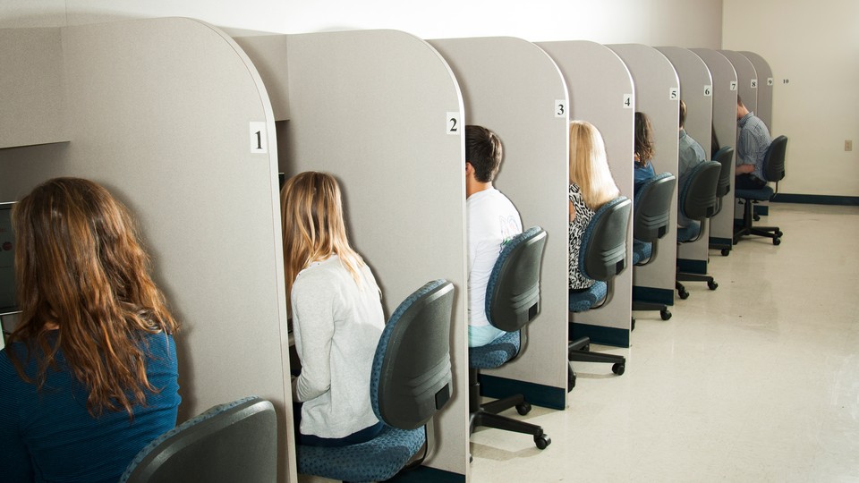 Picture showing nine teens sitting down in a line of nine cubicle desks.
