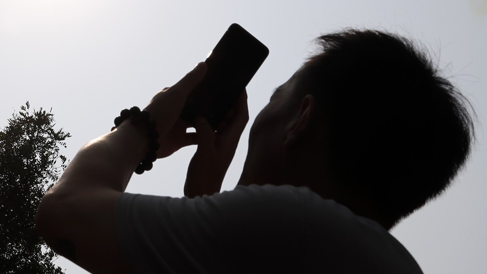 A backlit man points his cellphone toward the sky