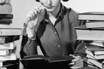 A woman reading a book surrounded by piles of books
