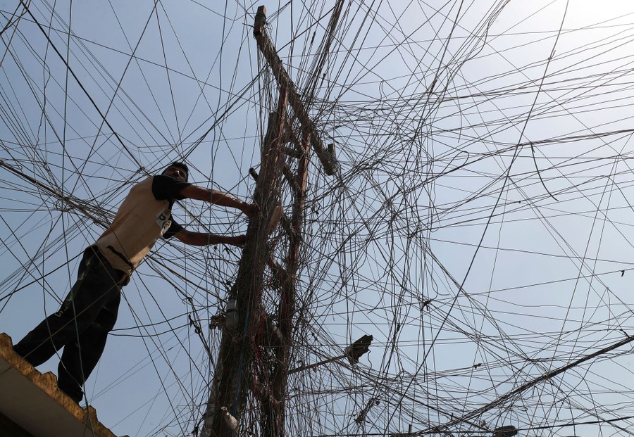 A man works on a power line, amid a dense tangle of other power lines.