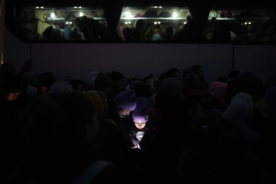 A night view of a crowd of people, with only a pair of faces lit up by a mobile device.