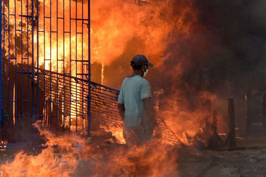 A person walks between flames, beside a damaged gate.