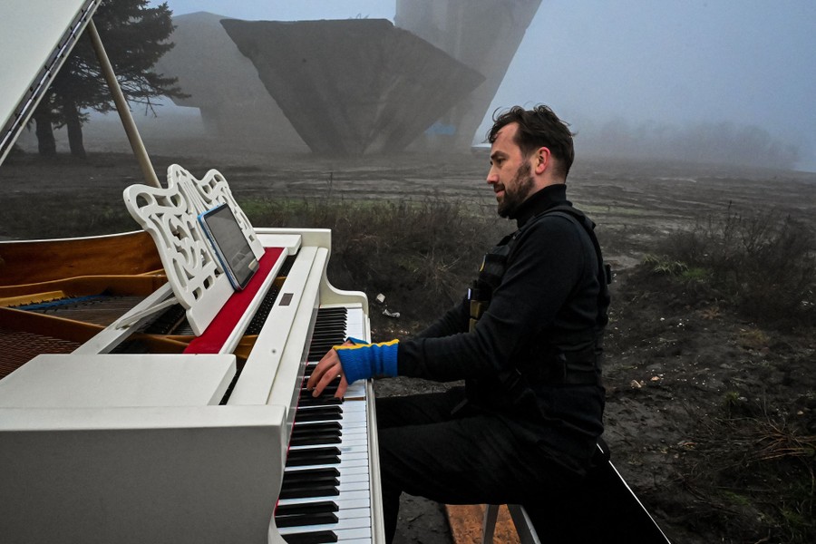 A person plays a piano outside on a foggy day, near a large concrete monument.