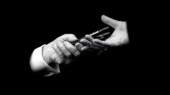 A black-and-white image of pens being exchanged from one hand to another