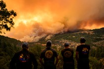 Firefighters watch as flames and smoke move through a valley in the Forest Ranch area of Butte County