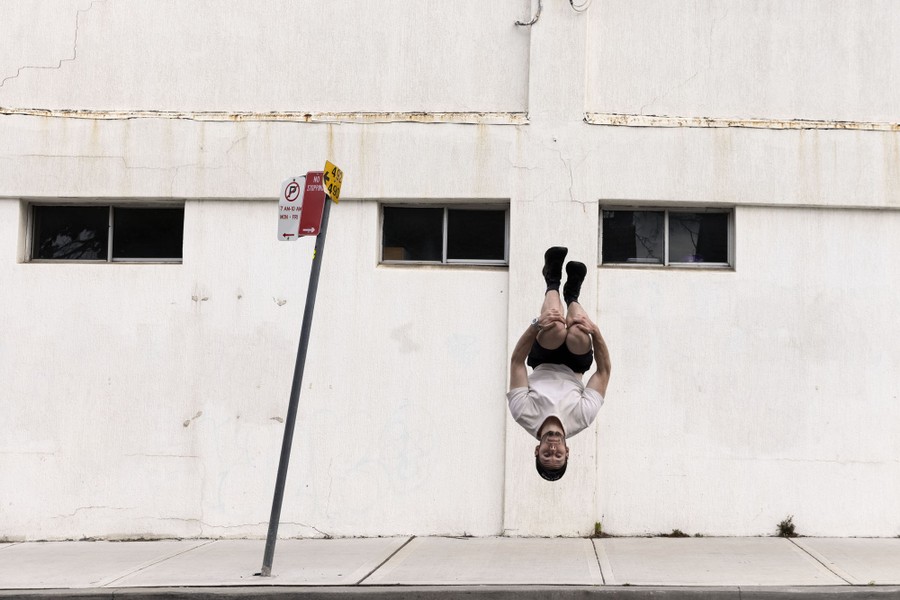 A young man flips in the air on a city street.