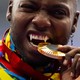 An athlete playfully bites a gold medal during a ceremony. Their canine teeth have been modified to look like long fangs.