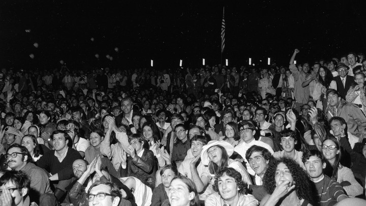 A group of people cheer with an American flag in the background.