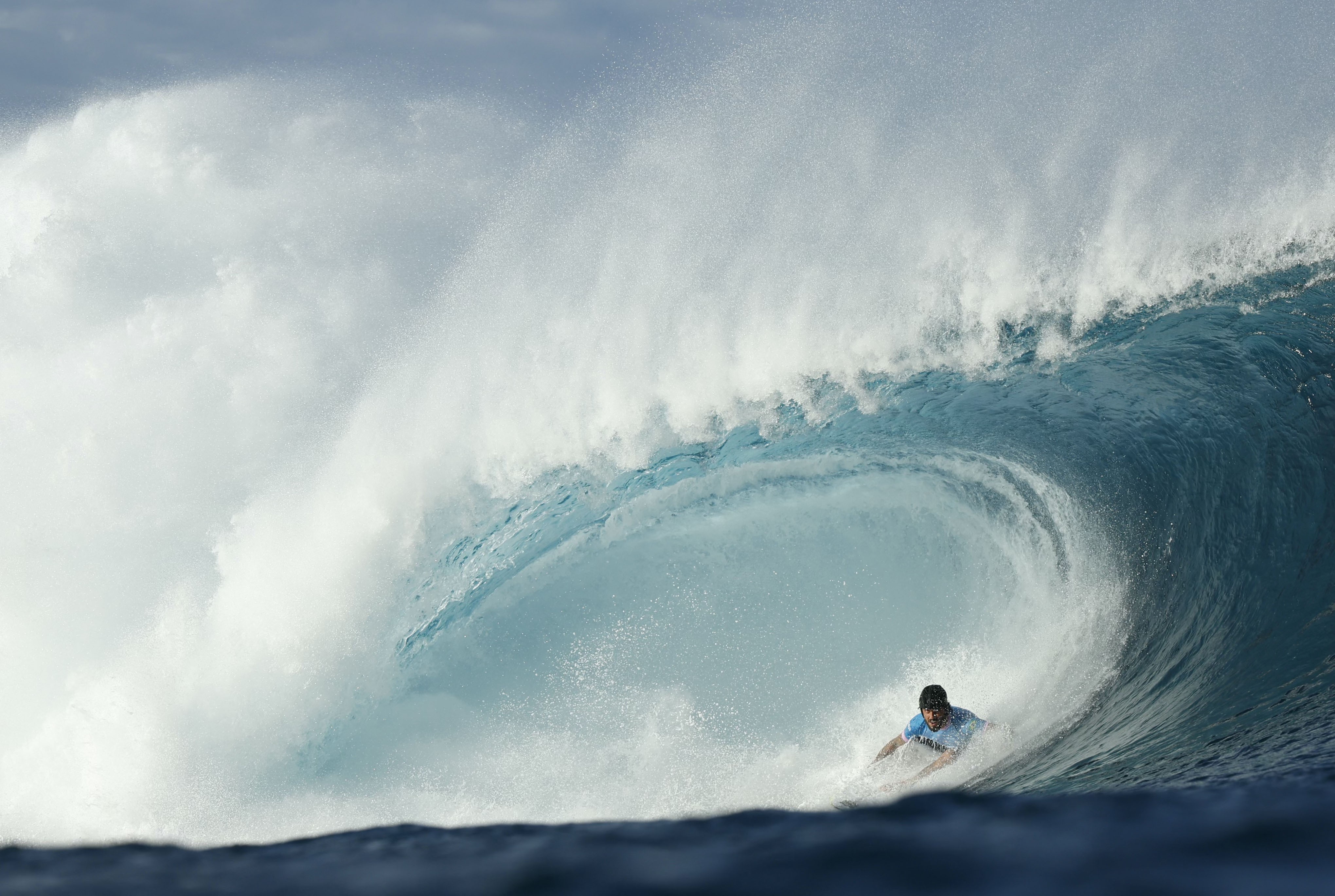 A surfer rides low inside the barrel of a huge breaking wave.
