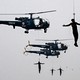 Four soldiers dangle from cables beneath flying helicopters.