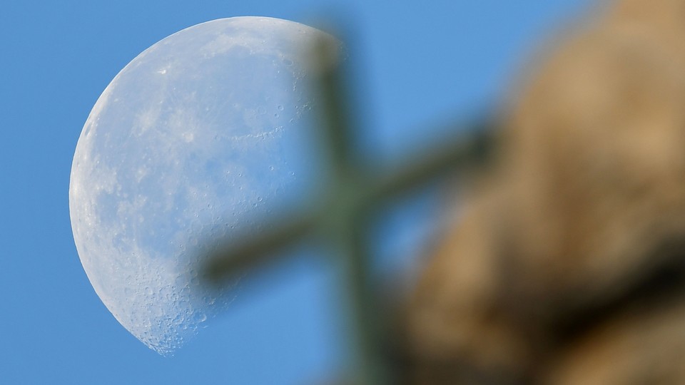 A large full moon sets behind a cross on Saint Peter's Basilica in November 2016.