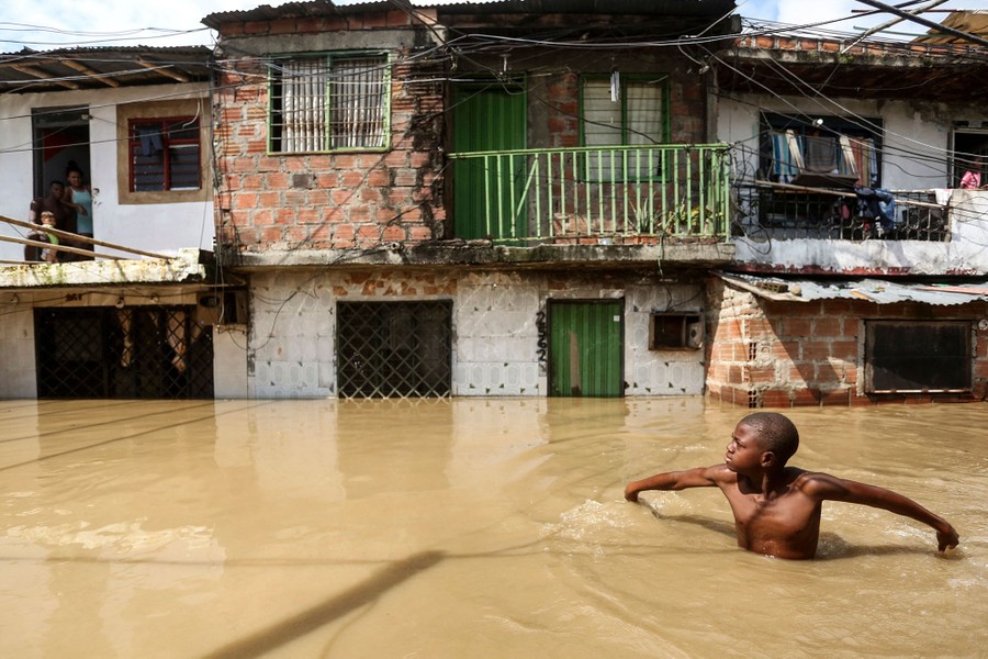 A boy walks through a flooded street in chest-deep floodwater.