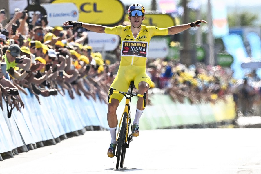 A cyclist raises his arms as he crosses the finish line, cheered on by fans.