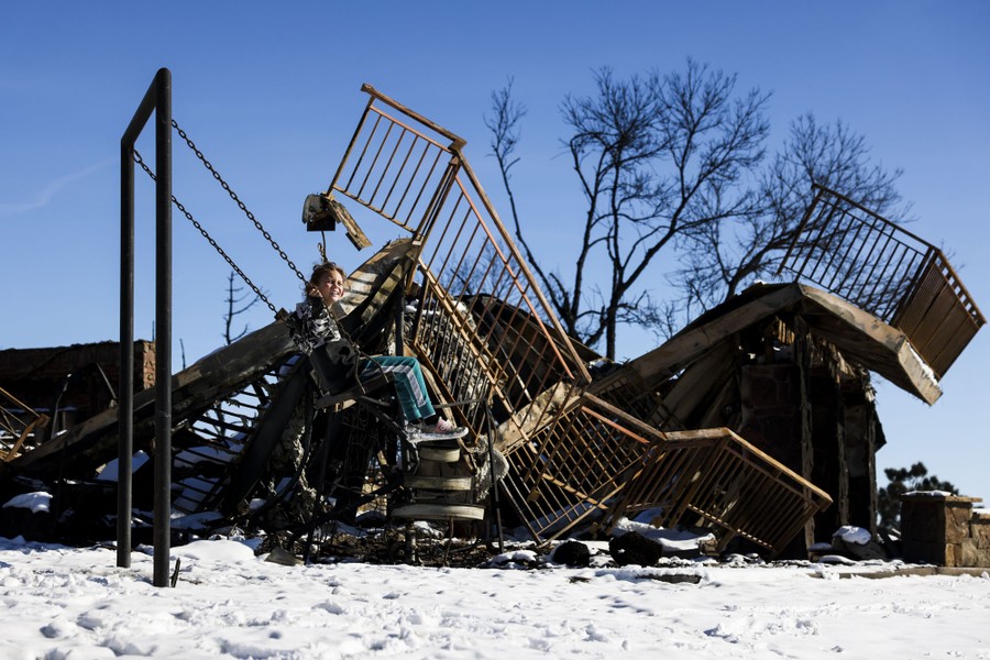 A child swings beside the ruins of a burned home.