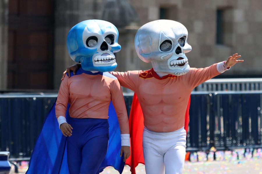 Performers dressed as wrestlers with giant skull heads take part in a parade.