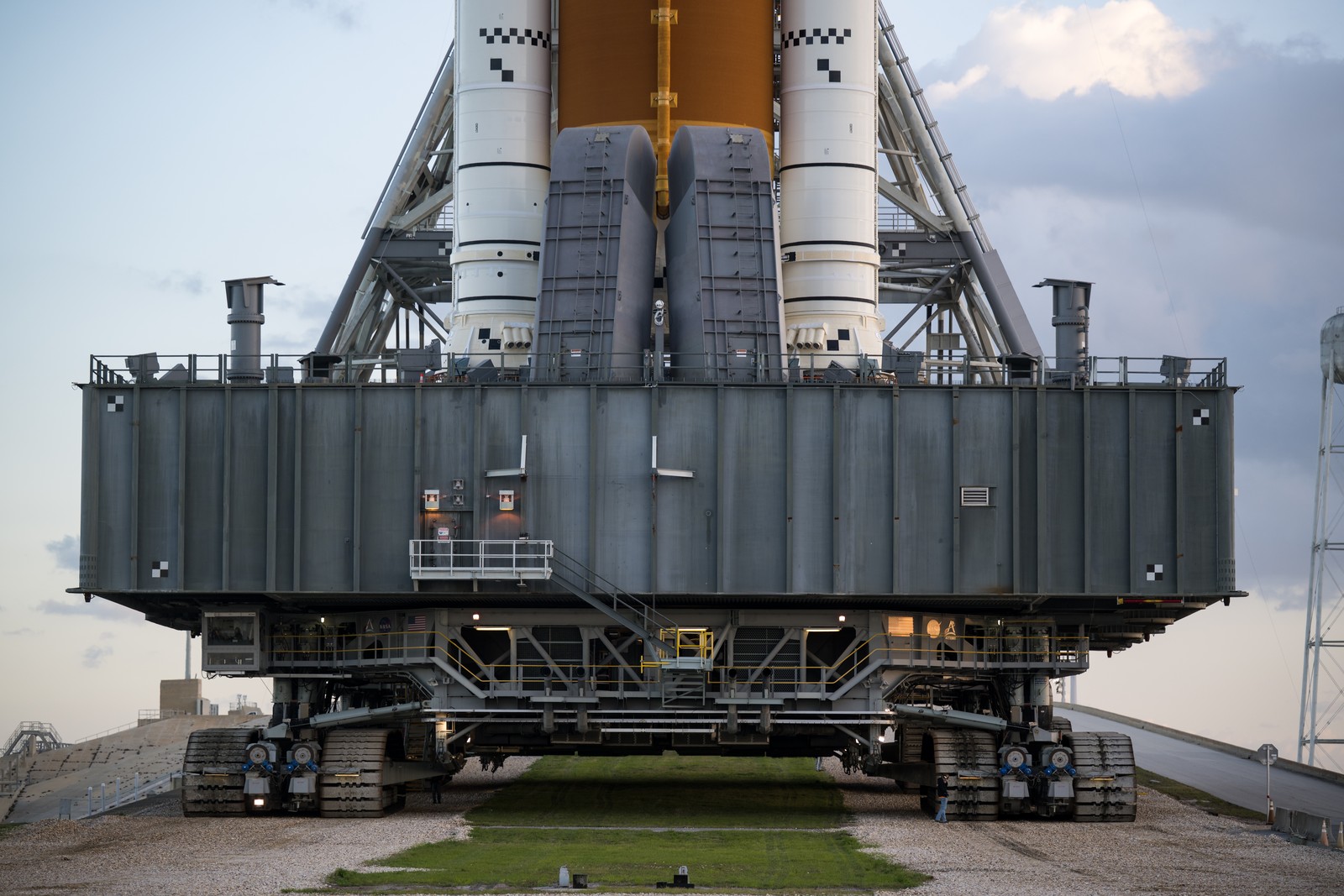 A massive tracked vehicle that acts as a platform carries a tall rocket to a launch pad.