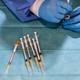 gloved hands load a vaccine into a syringe, next to an array of other vaccine syringes