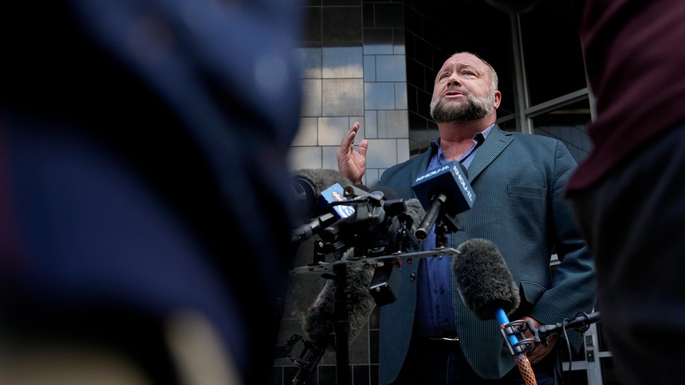 A photo of Alex Jones standing before microphones at a press conference outside a Houston courthouse