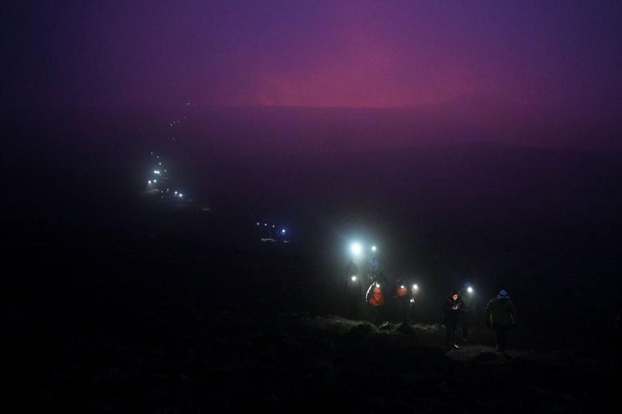 A line of dozens of people can be seen stretching to the horizon at night, visible by the light of their flashlights.