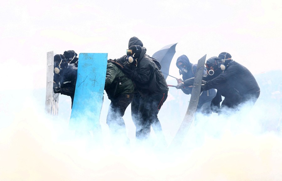 Several protesters hold shields in a cloud of tear gas.