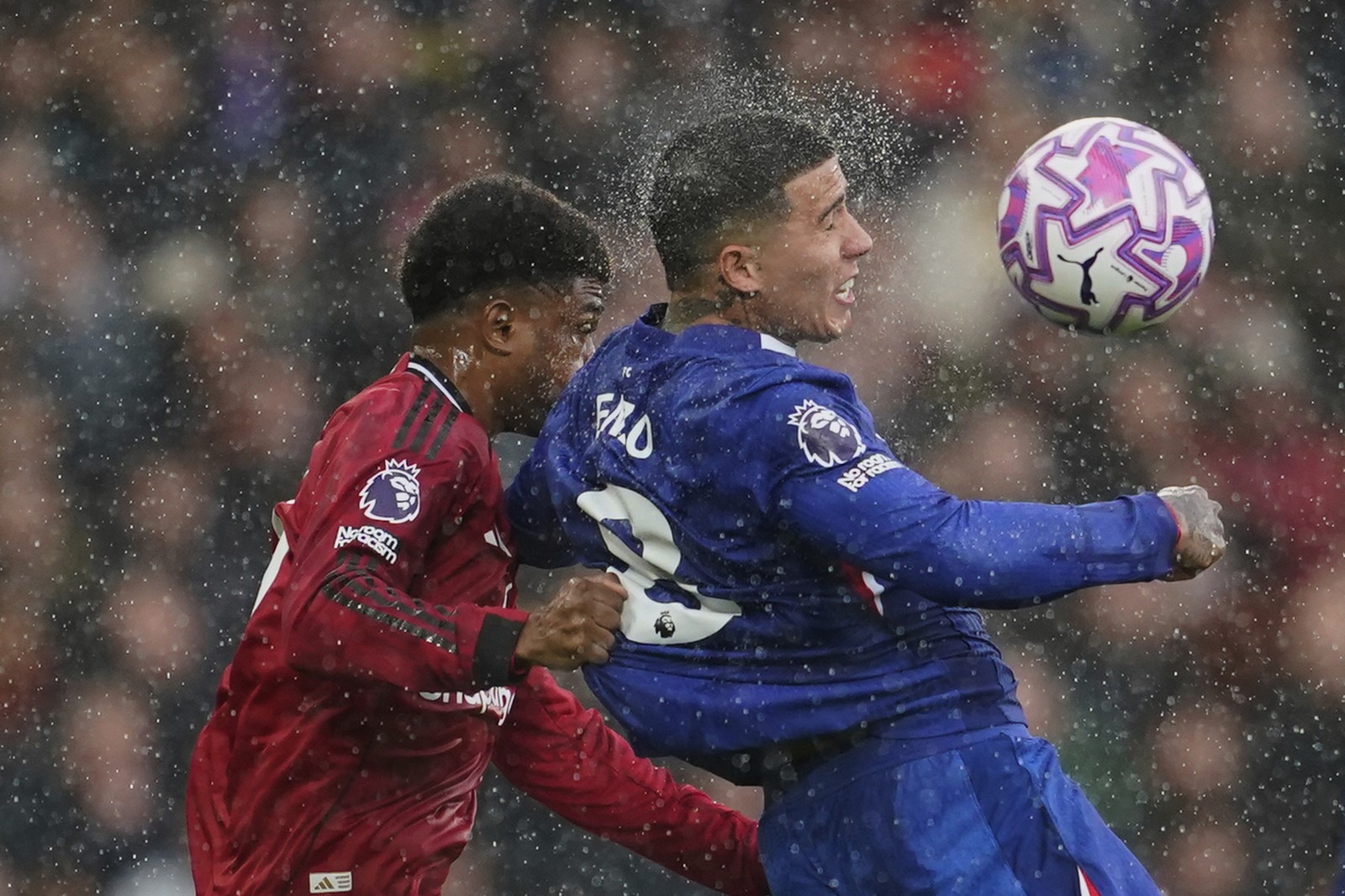 Two players compete for the ball at a soccer match, during a rainstorm.