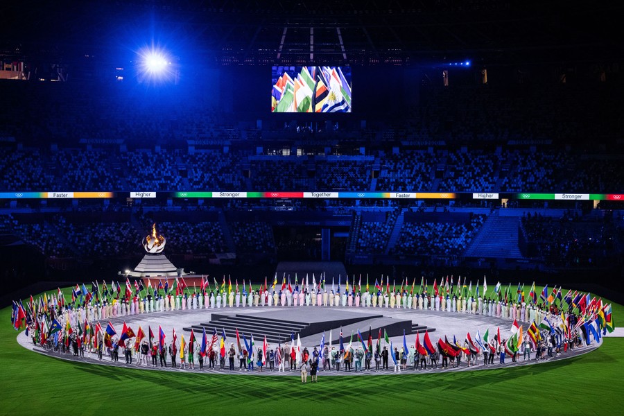 People stand in a large circle in a sports stadium, holding national flags.