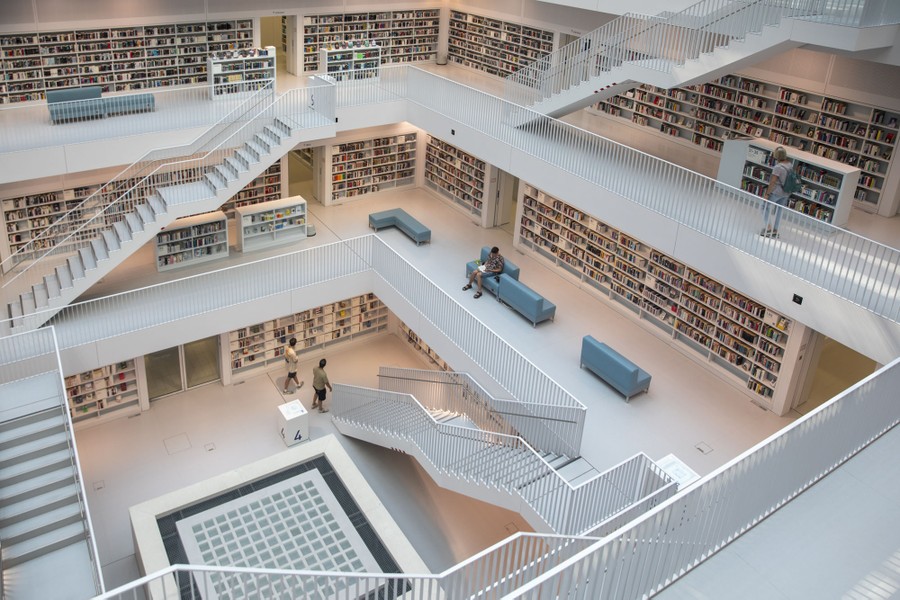An interior review of a brightly lit modern library, looking down into a broad atrium several stories high.