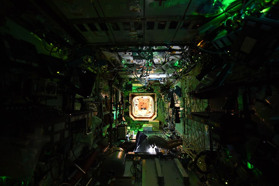 A dark interior view of the International Space Station, with many small lights from electronic components.