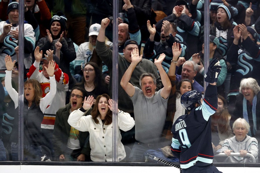 A crowd of hockey fans cheer rinkside.