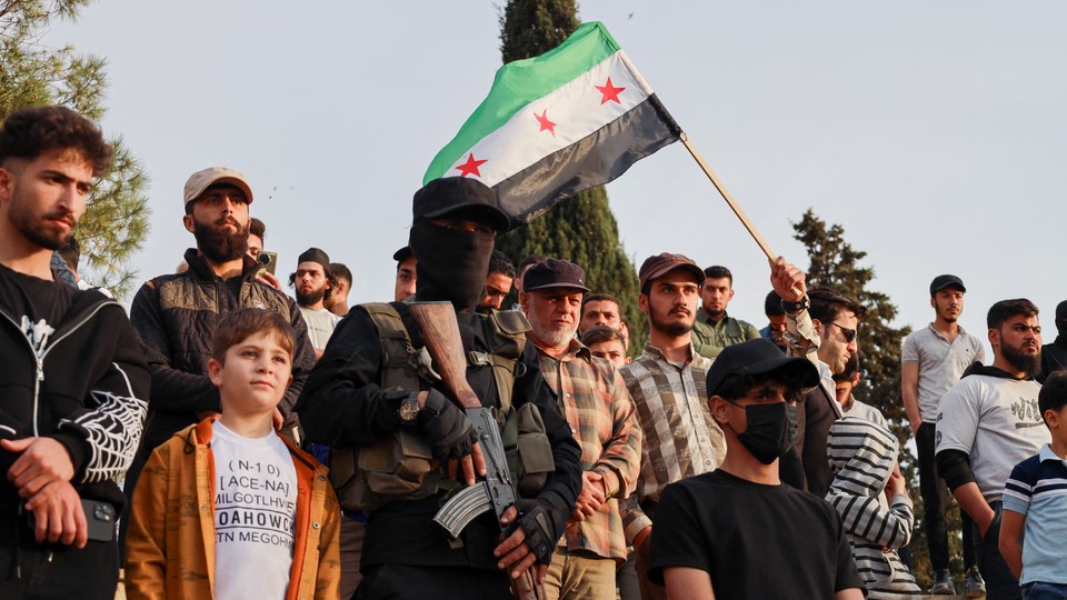 In Idlib, Syria, on May 4, protesters against Israeli strikes include a child, a man waving a Syrian flag, a masked gunman, and many others.