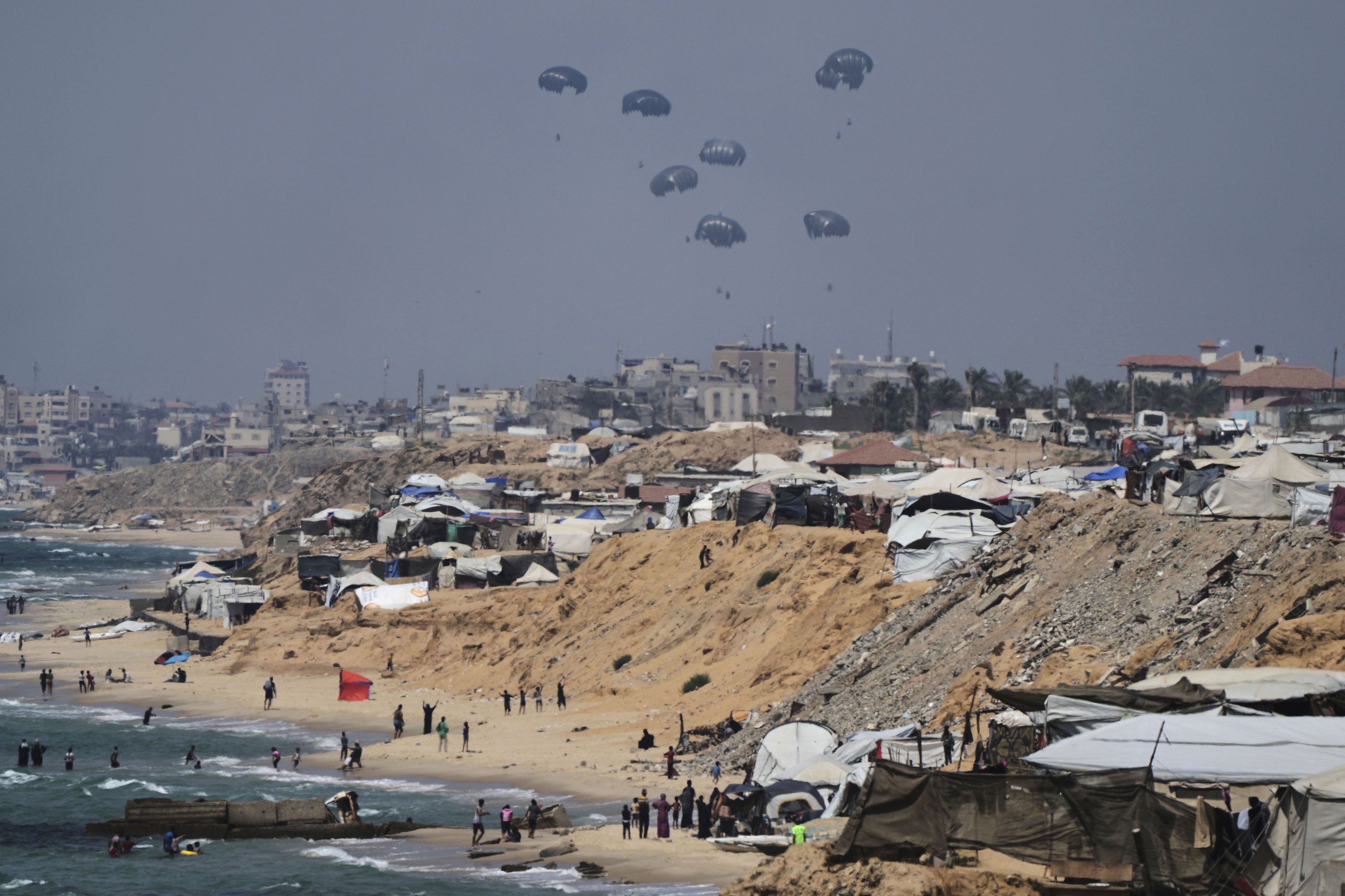 Nine or ten parachutes are seen descending over Gaza, carrying humanitarian aid.