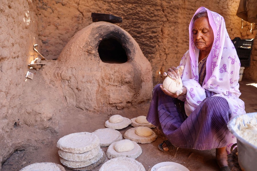 A woman works with dough, making loaves of bread outside.
