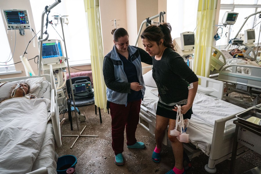 Vários pacientes em ambiente hospitalar, entre leitos.  Um está de pé, ajudado por outra pessoa.