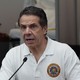 Andrew Cuomo in a white shirt in front of a microphone