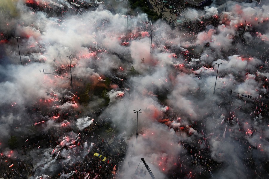 A large crowd of people gather in a square for a rally, with many holding lit torches that give off a lot of smoke.
