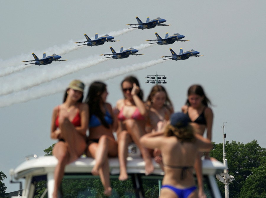 Six fighter jets fly in close formation above a group of women posing for a photograph.