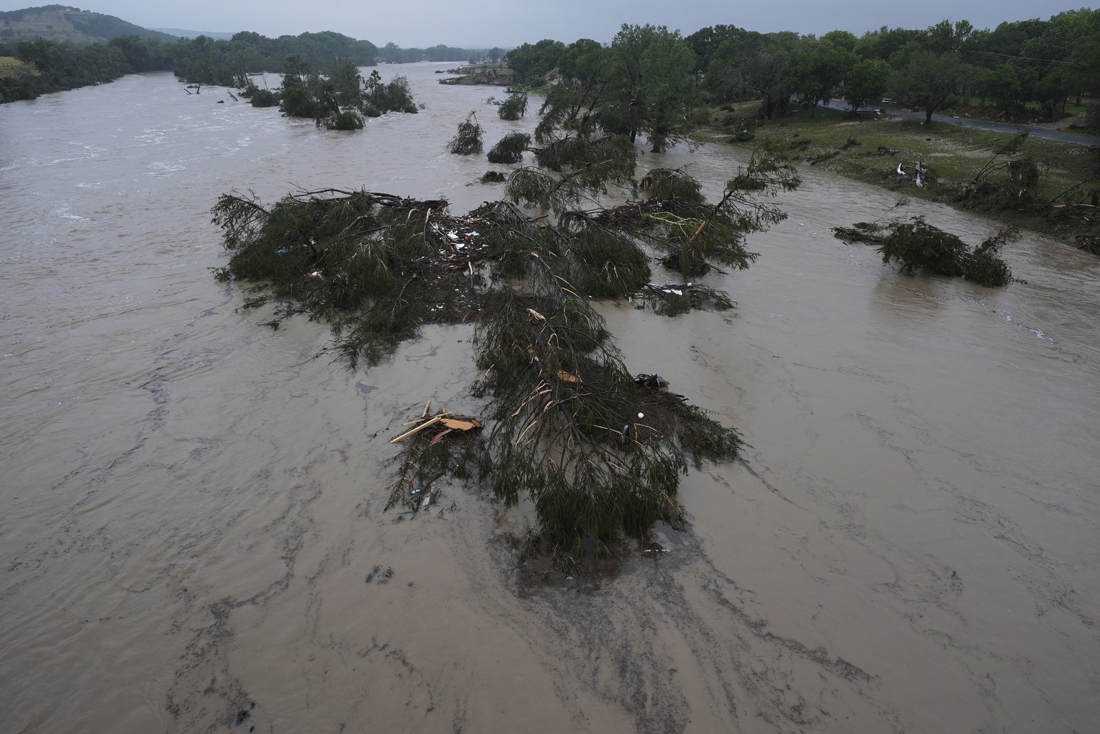 An aerial view of a muddy fast-flowing river littered with scattered debris and broken trees.
