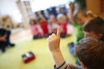 An unrecognizable kindergartener raises his hand