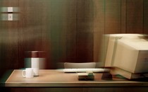 An empty desk with a boxy desktop monitor, keyboard, thermos, and coffee mug, with a stylized blur over it