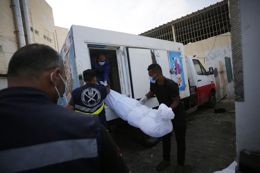 People lift a body, wrapped in a sheet, into the back of a refrigerated ice-cream truck.