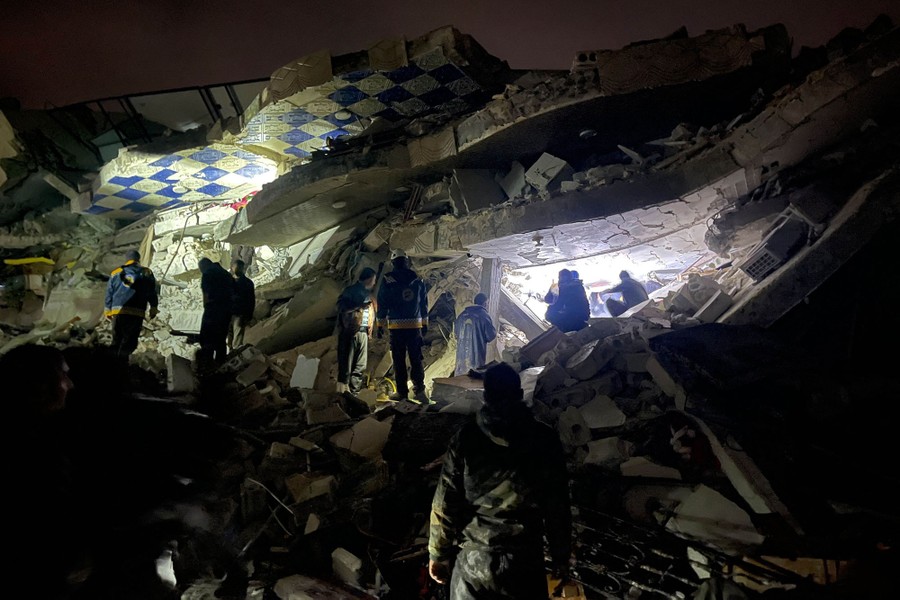 Rescuers stand on rubble using flashlights to look for victims.