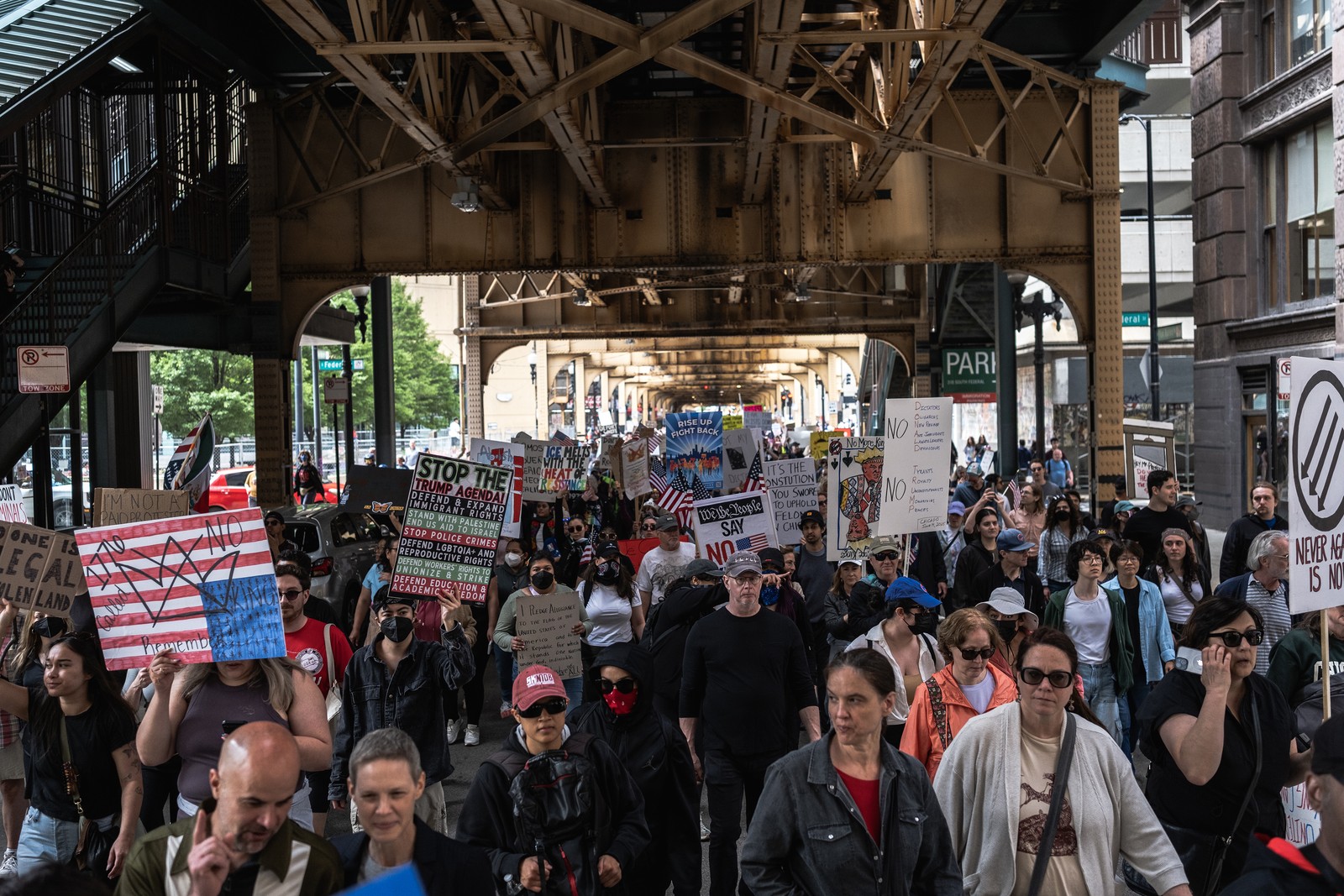 Protesters march down a street beneath an elevated railway.