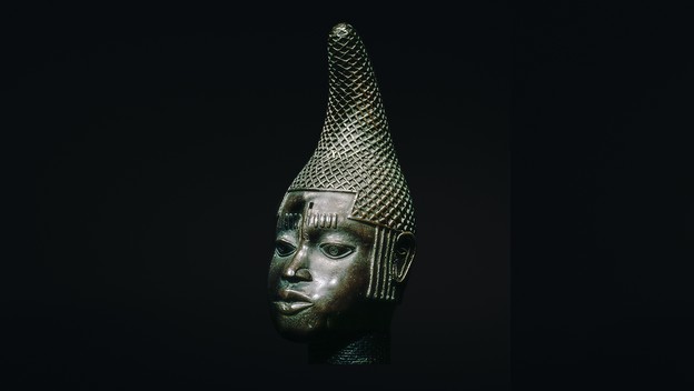 photo of a sculpture of a head with detailed conical headdress on black background