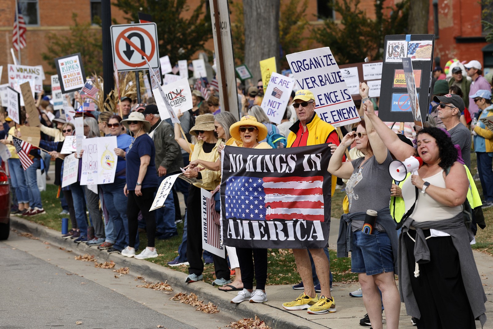 Protesters in a Michigan town stand along a sidewalk holding signs.