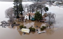 A two-story white house in California shown surrounded on all sides by muddy water halfway up its first level